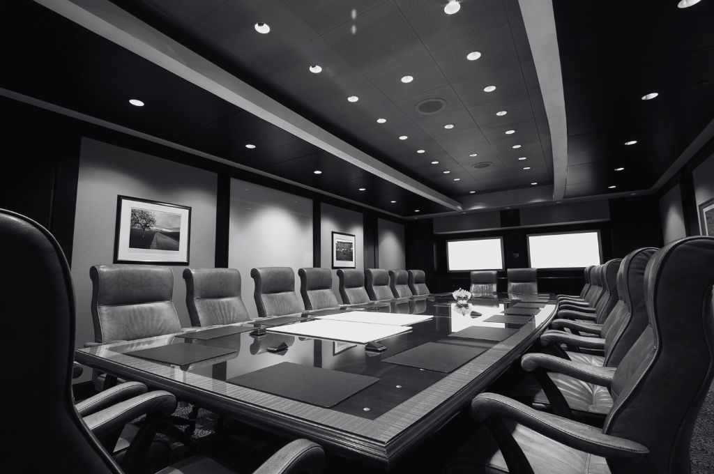 A photo of an executive boardroom with a long wooden table surrounded by leather chairs. Reveille Advisors provides HR teams, boards, and executive hiring committees with a variety of search and vetting services.