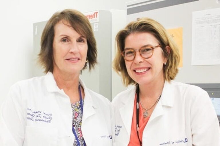 University of Kentucky's Drs. Sharon Walsh and Michelle Lofwall. Two women facing the camera wearing their white lab coats.